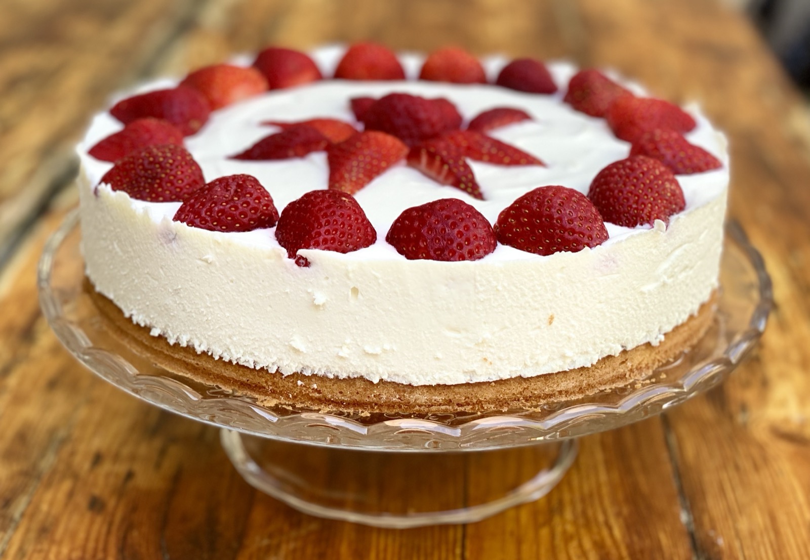 Strawberry cream cake on a glass cake stand showing the sponge base, quark cream layer and fresh strawberries on top