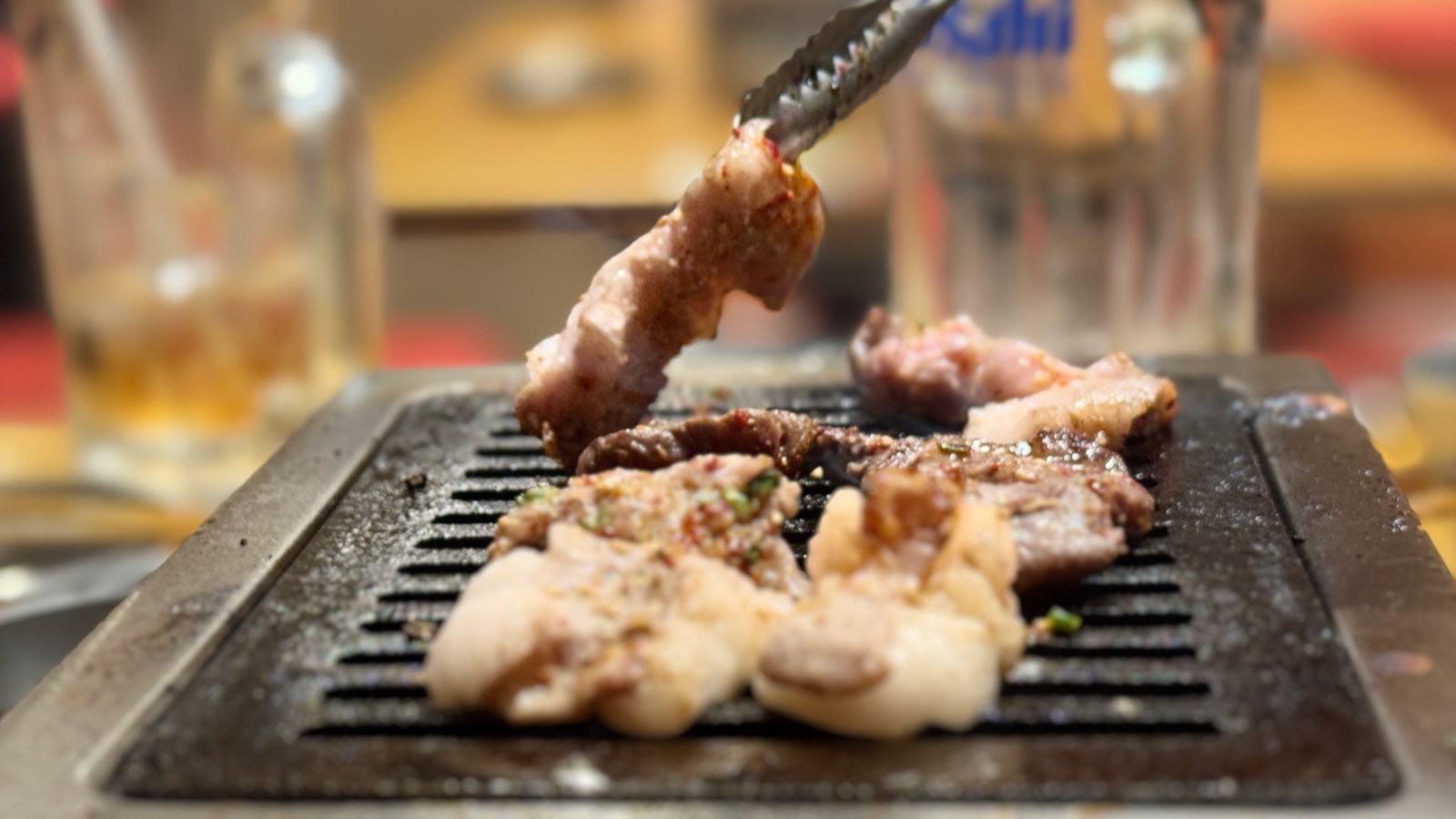 Yakiniku grill close-up — meat sizzling with tongs at Futago