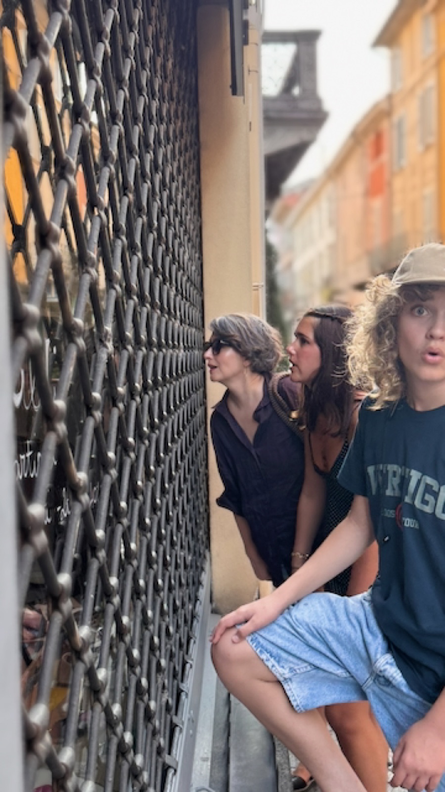 All three peering through a closed shop shutter in Crema — what does one do around here?