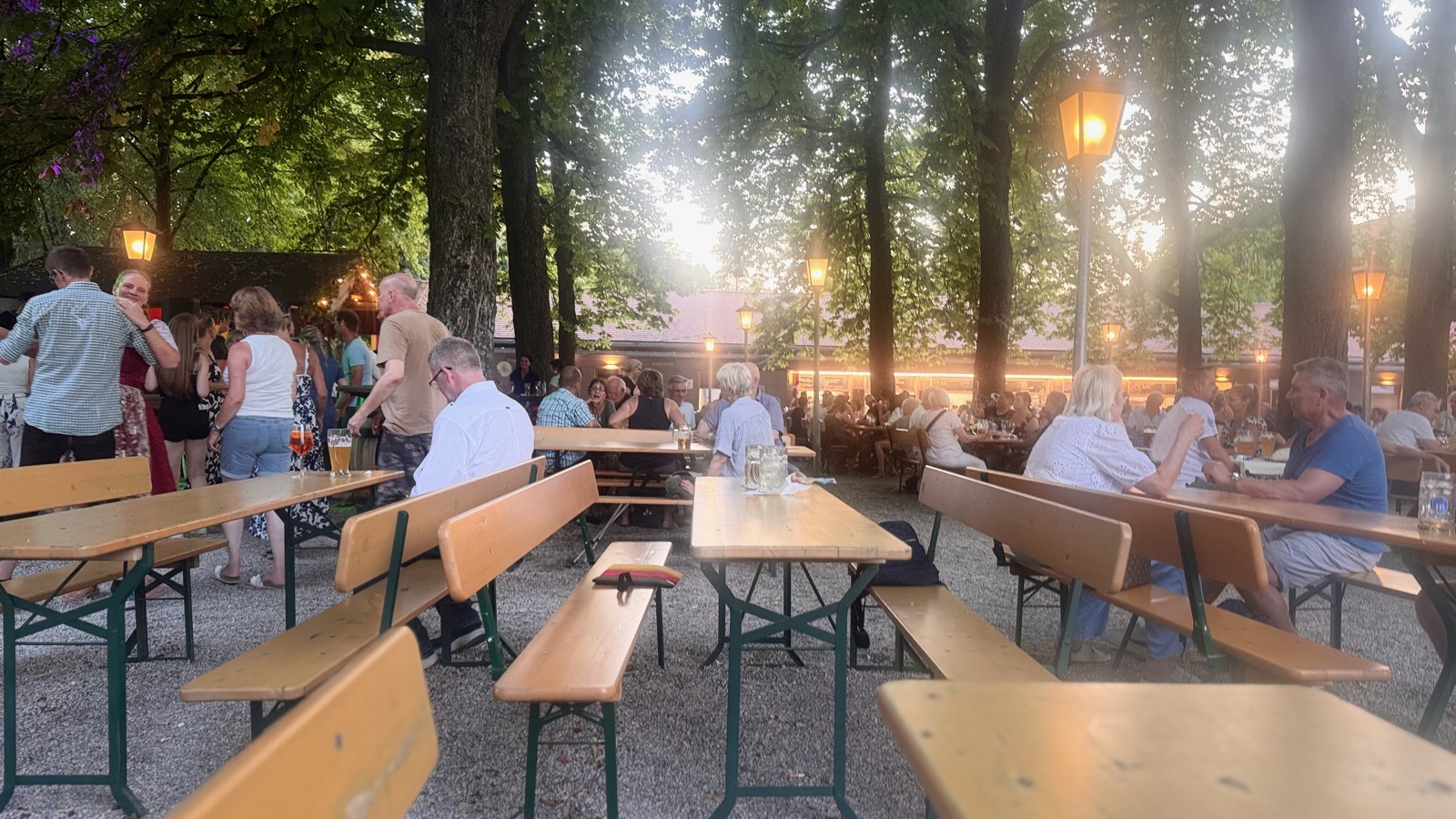Beer garden at dusk, lanterns lit, dancing by the trees